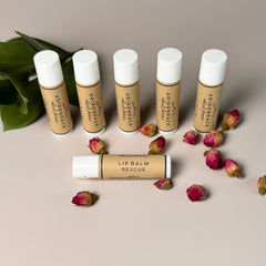 Lip balm tubes with white caps, brown labels, and Adirondack Natural Skincare branding, with dried roses