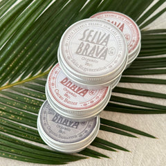 Organic skin care products in silver tins, stacked with visible brand names, on green leaves