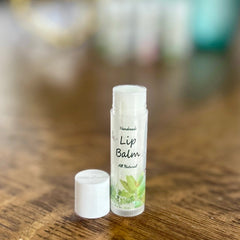Lip balm tube with white cap, clear label, and green leaf design on wooden surface