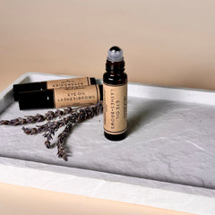 Eye oil bottle with brown glass, tan label, and silver rollerball top on a white tray