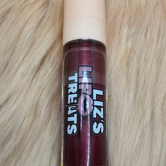 Lip gloss tube, dark red with glitter, white cap, "Liz's Treats" label on fur background
