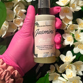Jasmine glow oil with glitter, held by pink gloved hand, surrounded by white flowers