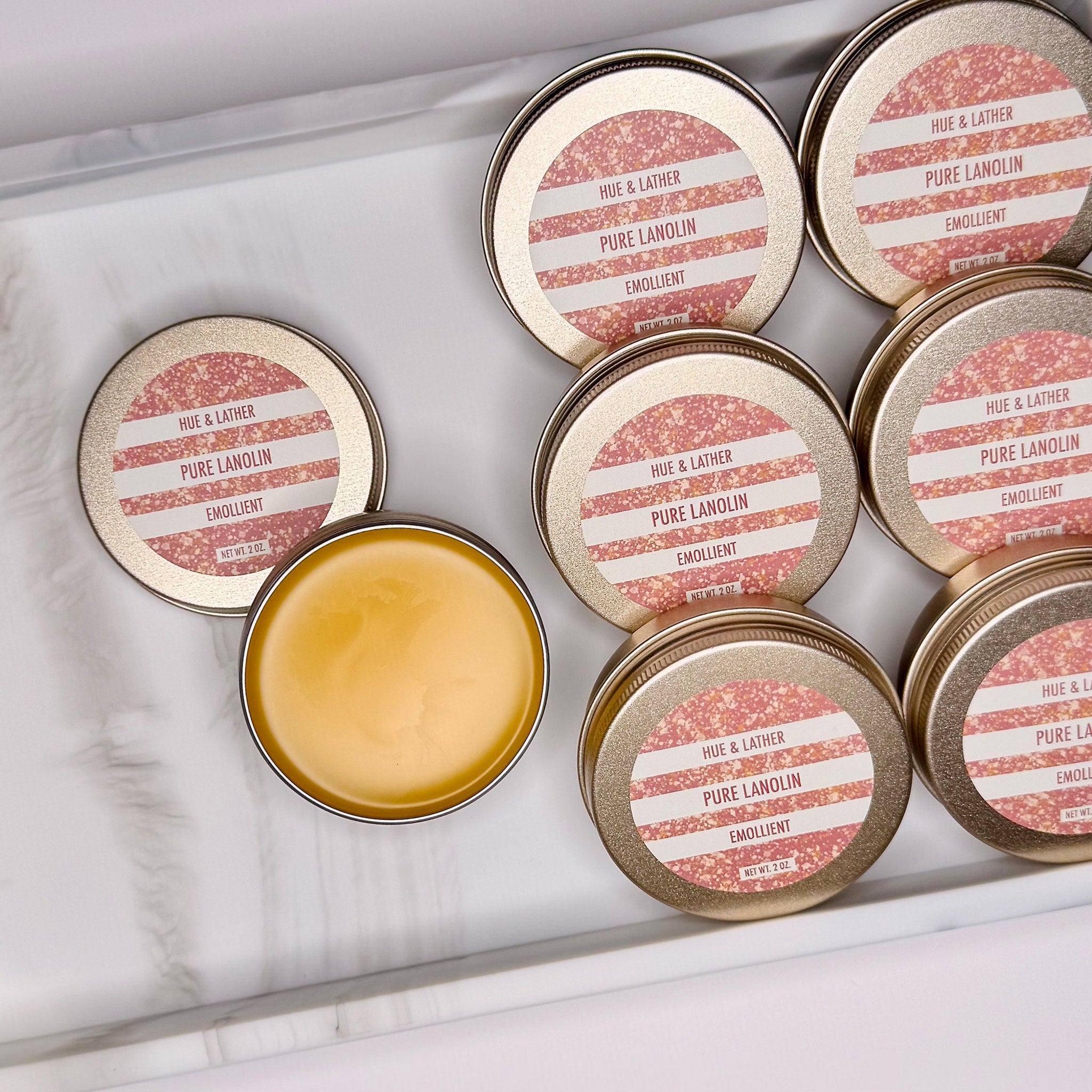 Pure Lanolin tins with gold lids, pink label, and yellow balm, Hue & Lather brand
