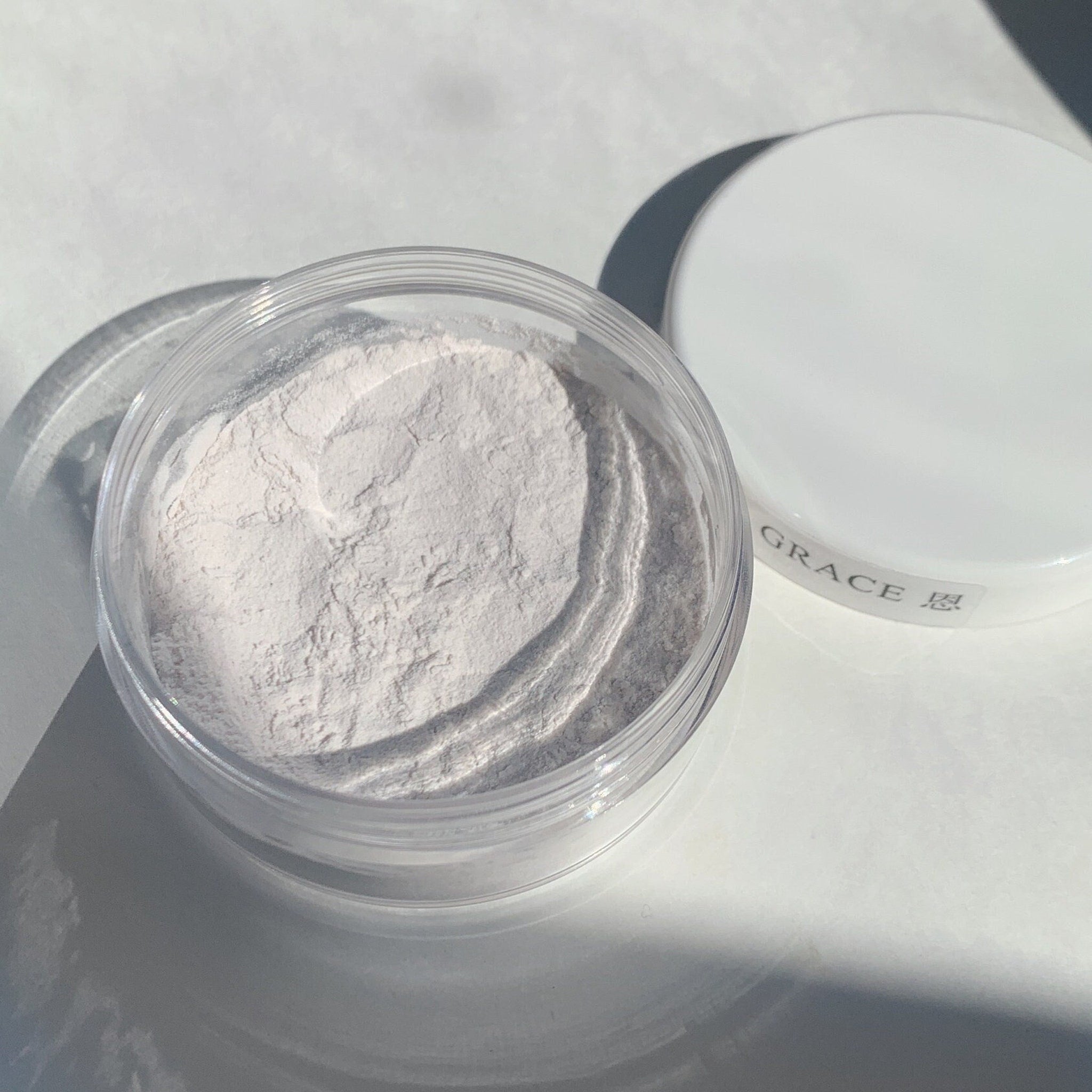 Face powder in clear plastic jar, light beige powder, white lid with "GRACE" text
