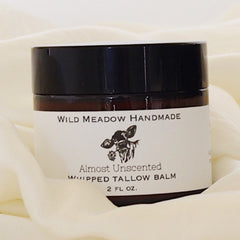 Side view of golden whipped tallow balm in sleek jar with black lid, showcasing rich texture