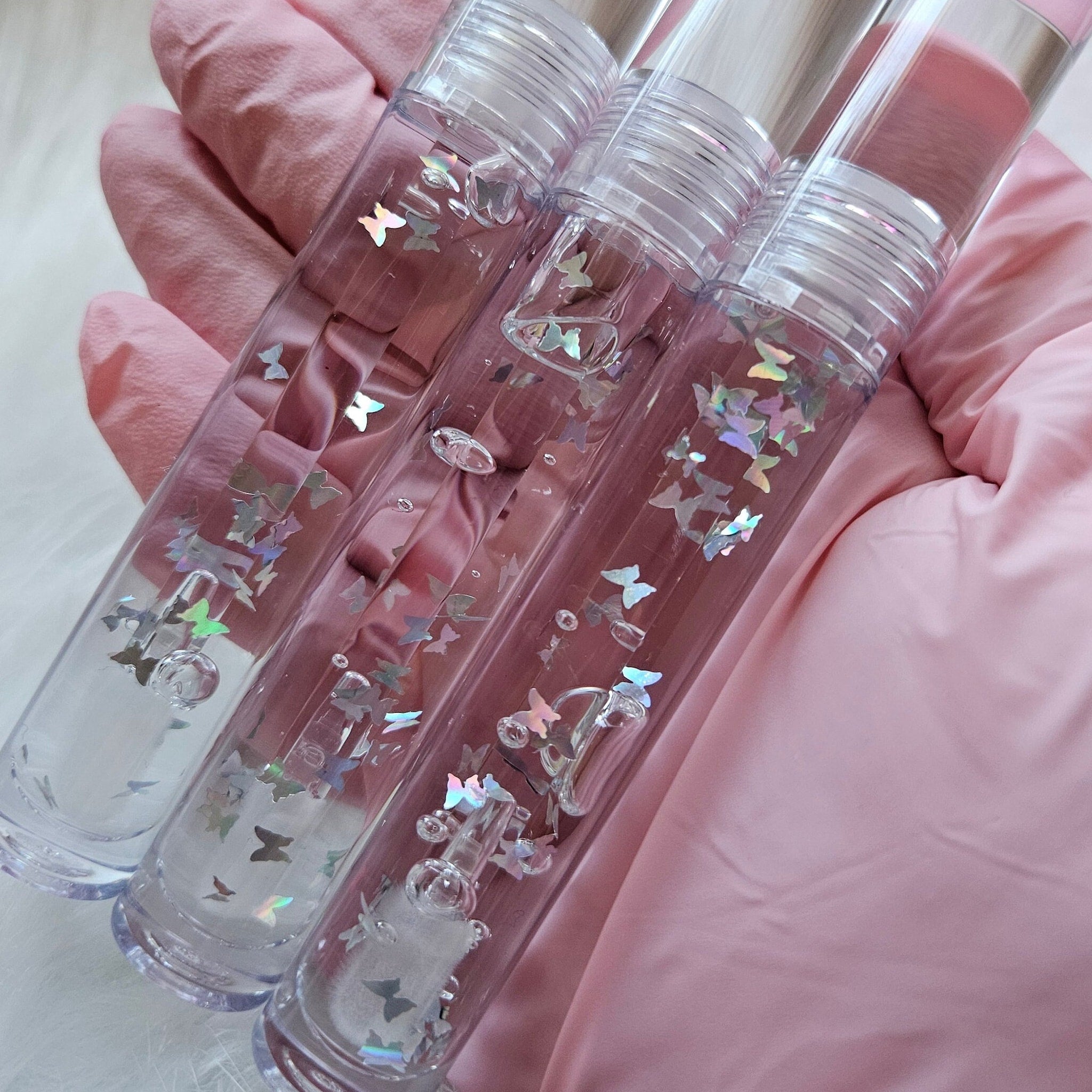 Clear lip gloss with butterfly glitter in clear tubes held in pink gloved hand