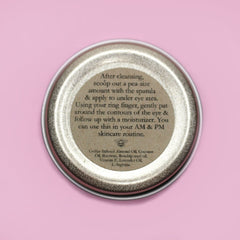 Eye cream container with silver metal lid, beige label, and text instructions for use on pink background
