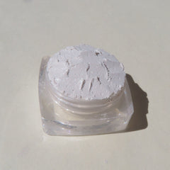 Side view of loose mineral eyeshadow in soft white with shimmer, showcasing powder texture in clear container