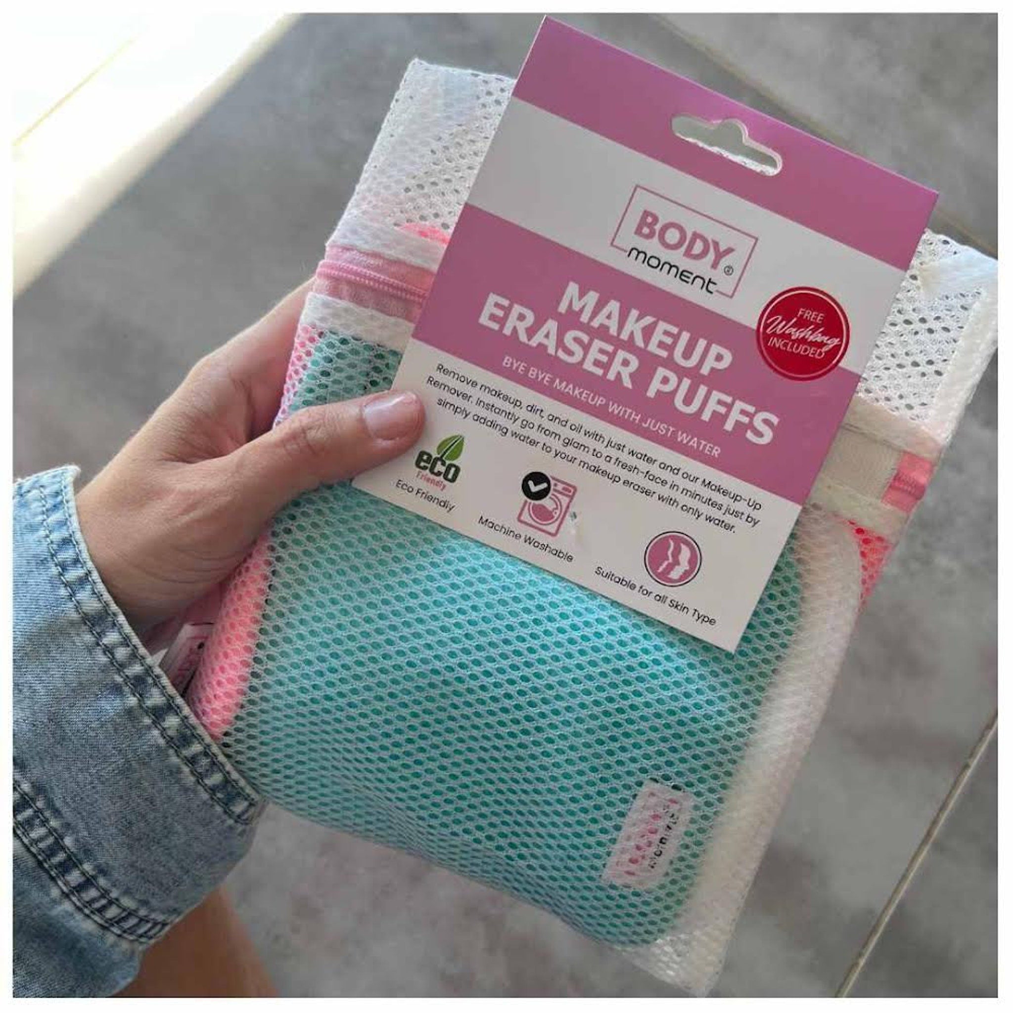 Makeup Eraser Puffs, pink and teal mesh cloths with white wash bag, held in hand with Body Moment packaging