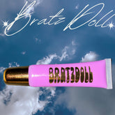 Lip gloss tube, pink and gold, with Bratz Doll text, against a blue sky background
