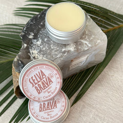 Cacao butter tins with silver lids, brown text, and SELVA BRAVA branding on a stone with green leaves