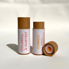 Lip balm tubes in brown cardboard with white labels, "Colorful Harvest" text, and mango illustration