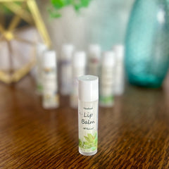Lip balm tube with white cap, green label, and "Lip Balm" text on wooden surface