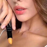 Lip balm with black tube and orange balm, held near lips