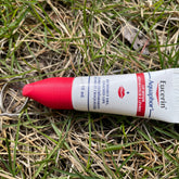 Lip balm tube with red cap, white tube, and Eucerin Aquaphor branding on grass