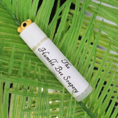 Lip balm tube with white label, yellow bee top, and The Humble Bee Soapery text on green leaf background