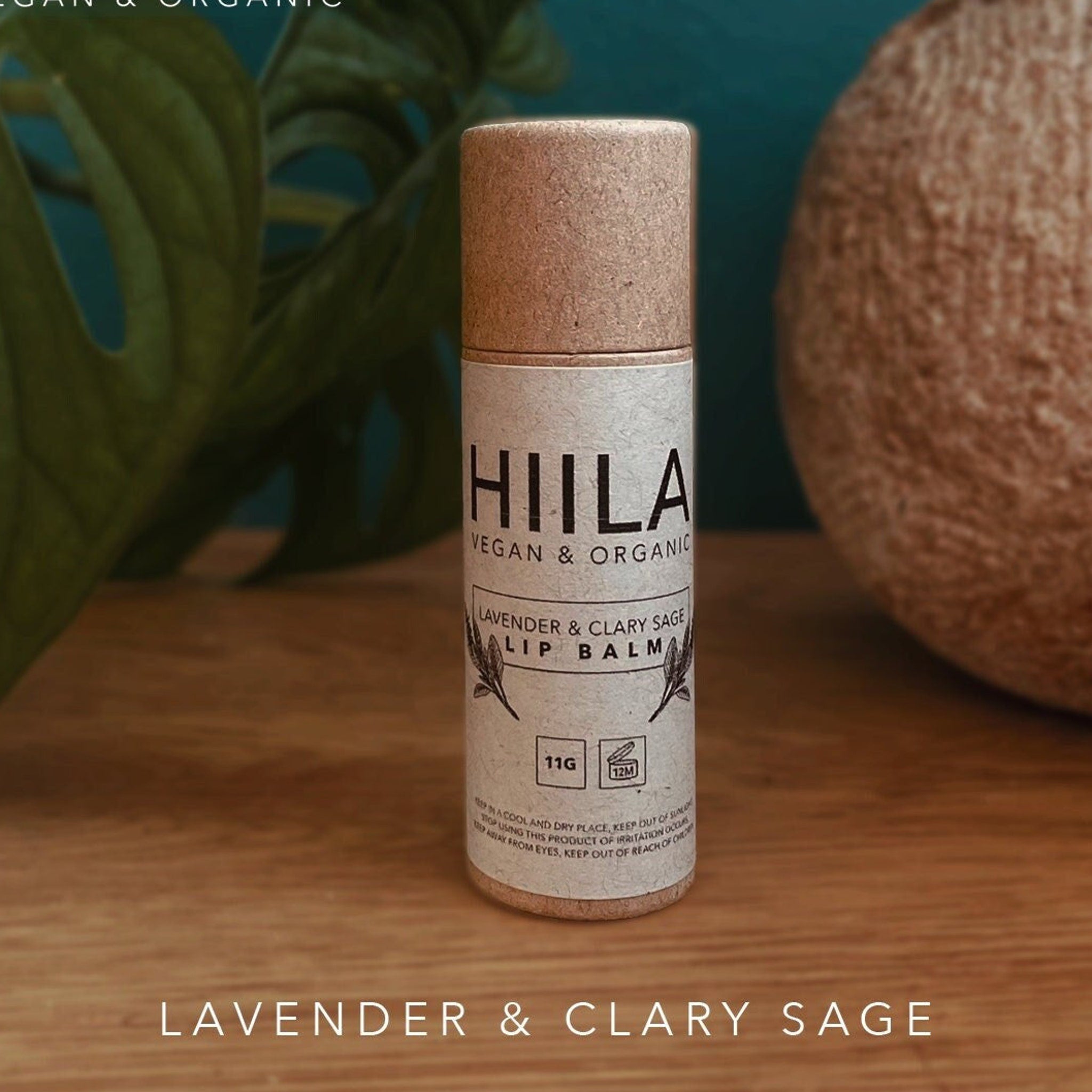 Lip balm tube with brown cap and HIILA label, on wooden surface, with plant in background