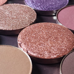 Close-up of makeup brush applying shimmery bronze eyeshadow from palette onto eyelid