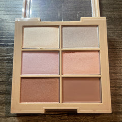 Eyeshadow palette with neutral shades of pink, beige, and brown in a square compact