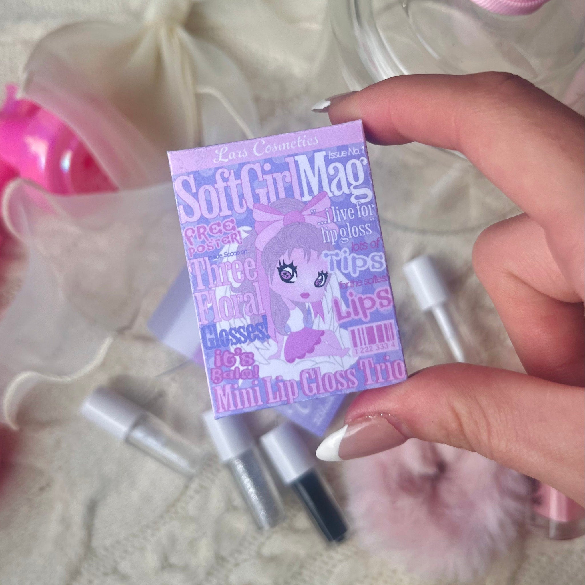 Mini lip gloss trio in purple packaging with Lars Cosmetics branding, held by hand, with other makeup items around