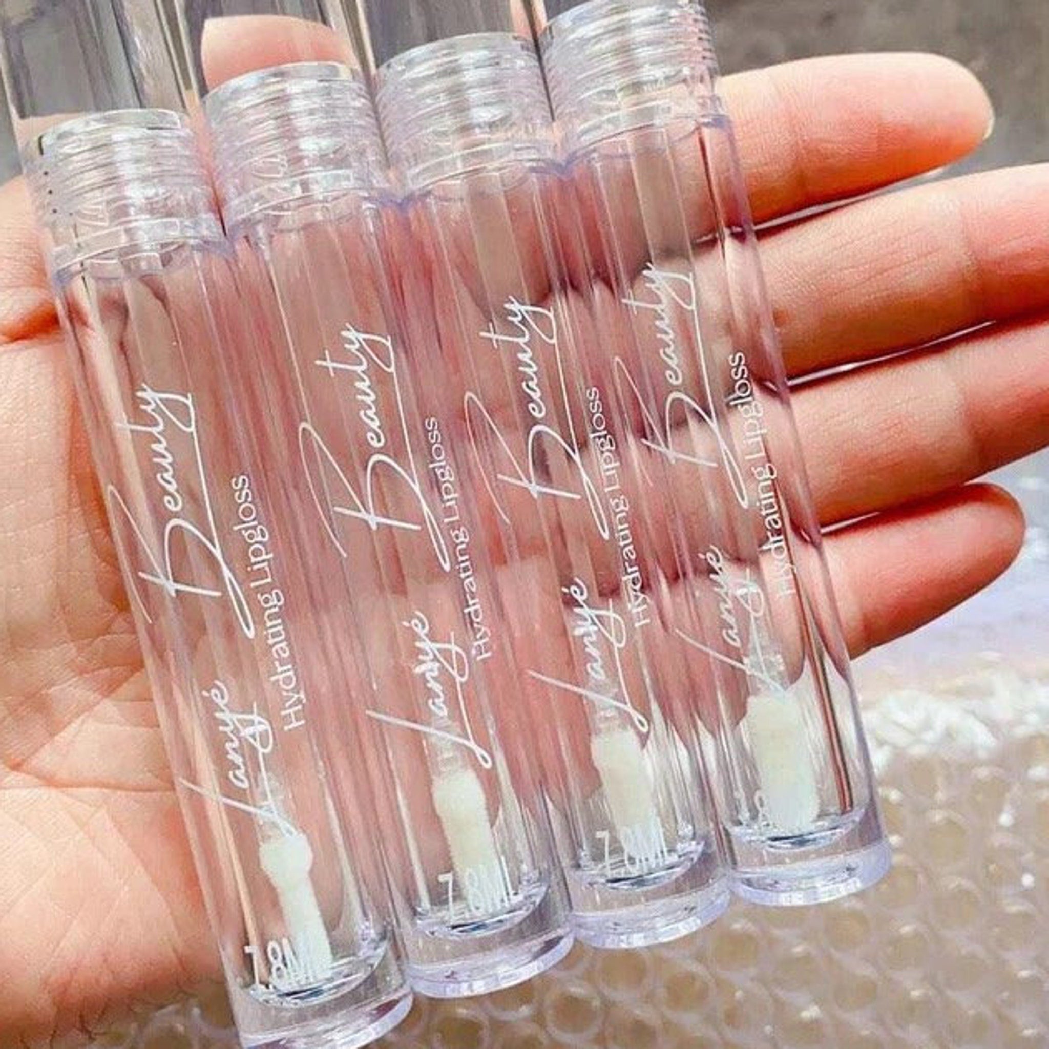Empty lipgloss tubes, clear plastic, white text, held in hand
