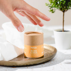 Balance cleanser cylinder with orange label, brown paper, and hand reaching towards it