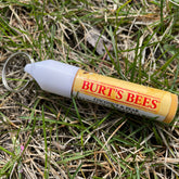 Chapstick holder with Burts Bees branding, yellow and white, with keyring in grass
