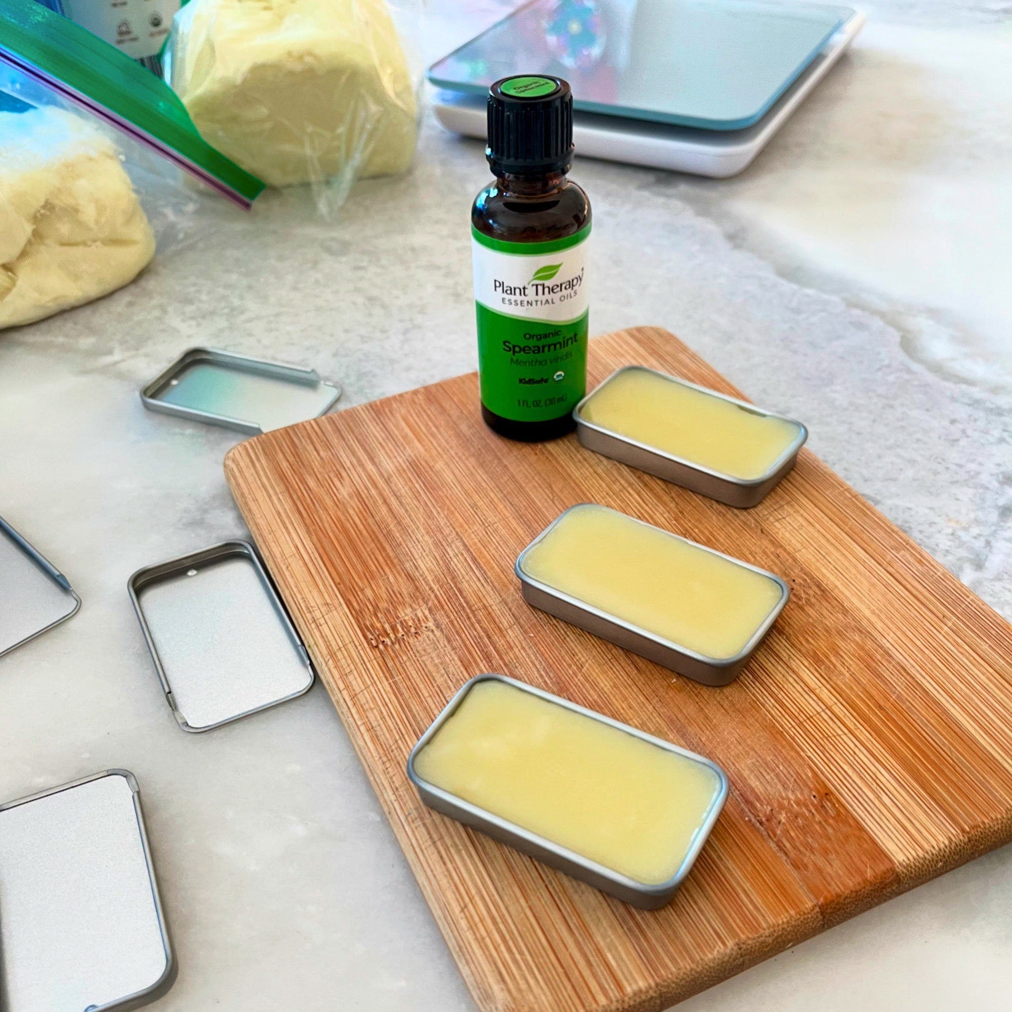 Lip balm tins with yellow balm on a wooden board, Plant Therapy essential oil bottle