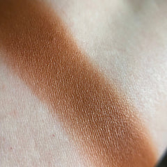 Hand applying auburn eyeshadow with a blending brush, showcasing rich warm tones on skin
