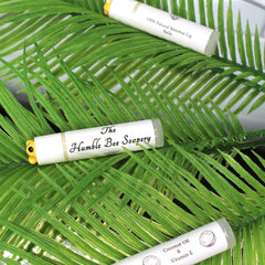 Lip balm tubes, white with black text, resting on green leaves, "The Humble Bee Soapery" visible