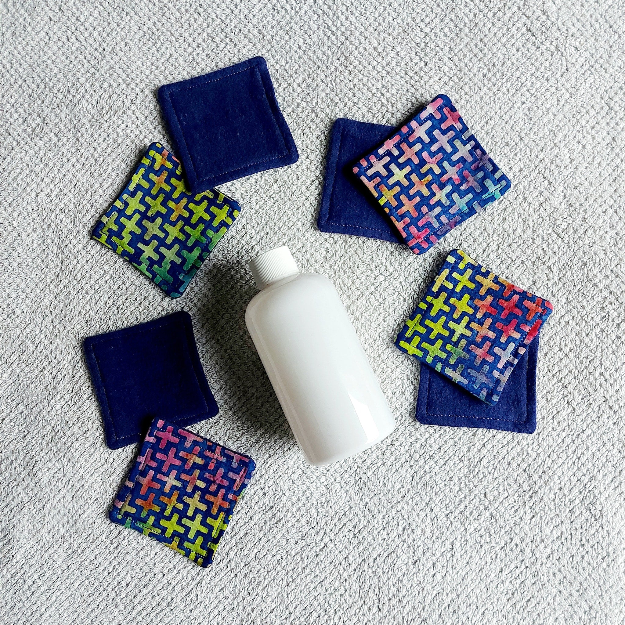 Makeup remover pads, navy blue and geometric patterned fabric pads, with a white bottle on a towel
