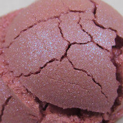 Hand applying light cerise pink shimmer eyeshadow with blue duochrome effect using a fluffy brush