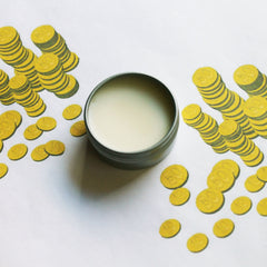 Lip balm in metal tin with white balm, surrounded by yellow coin illustrations on white background