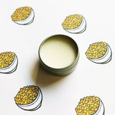Lip balm tin with silver metal, light yellow balm, and mac and cheese illustration pattern
