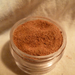Powdered spice in a clear plastic container with brown granules and a beige background