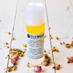 Facial cleanser bottle with yellow liquid, white cap, and Herba brand label on a white wooden surface with flowers.