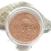 Adzuki facial scrub in clear plastic container, light brown powder, and grey rock background