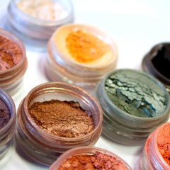Close-up of rich bronze eyeshadow powder in a round glass jar with gold lid, showcasing shimmering pigment texture