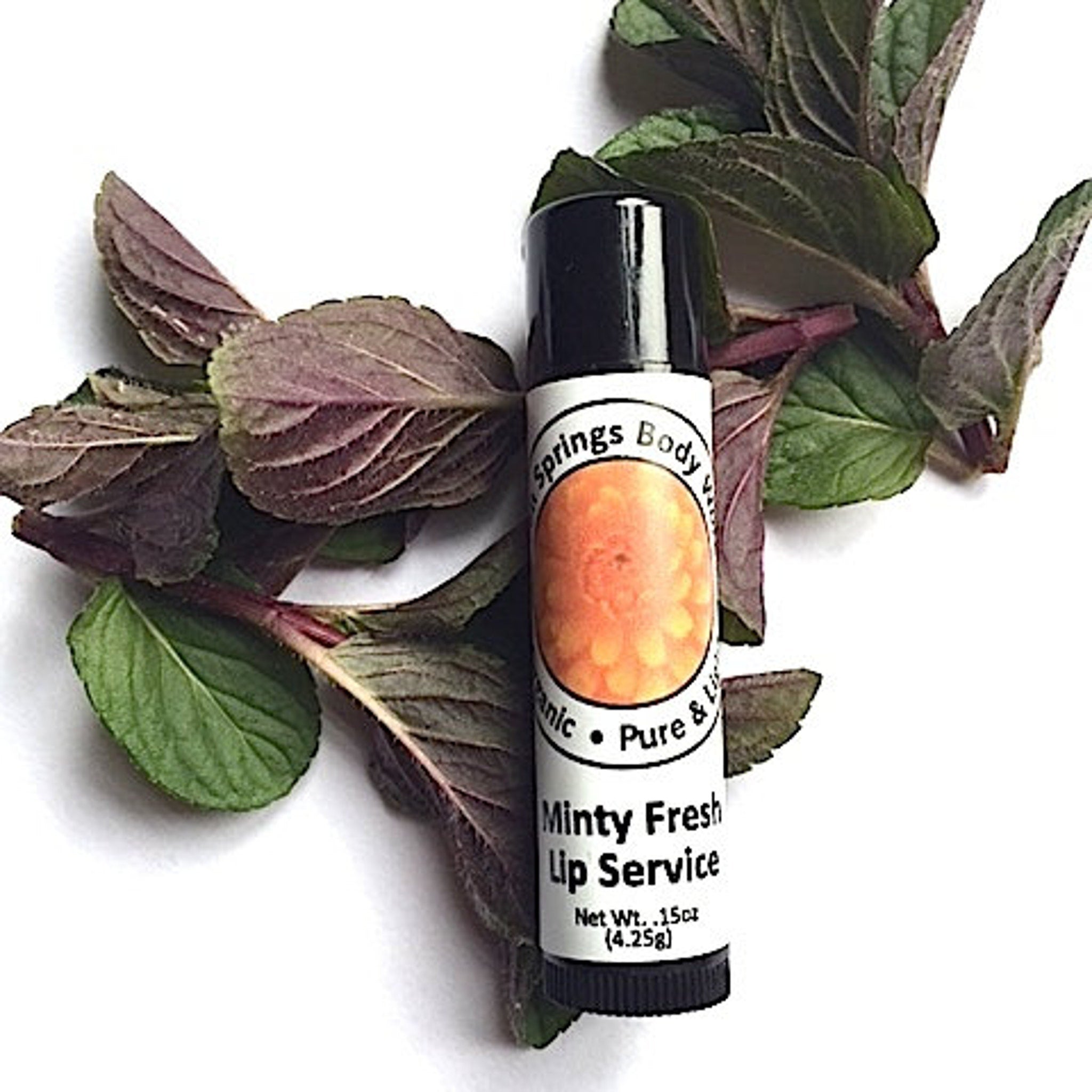 Lip balm tube with black cap, white label, and green and purple leaves around it
