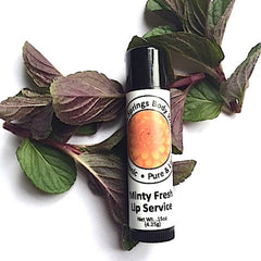 Lip balm tube with black cap, white label, and green and purple leaves around it