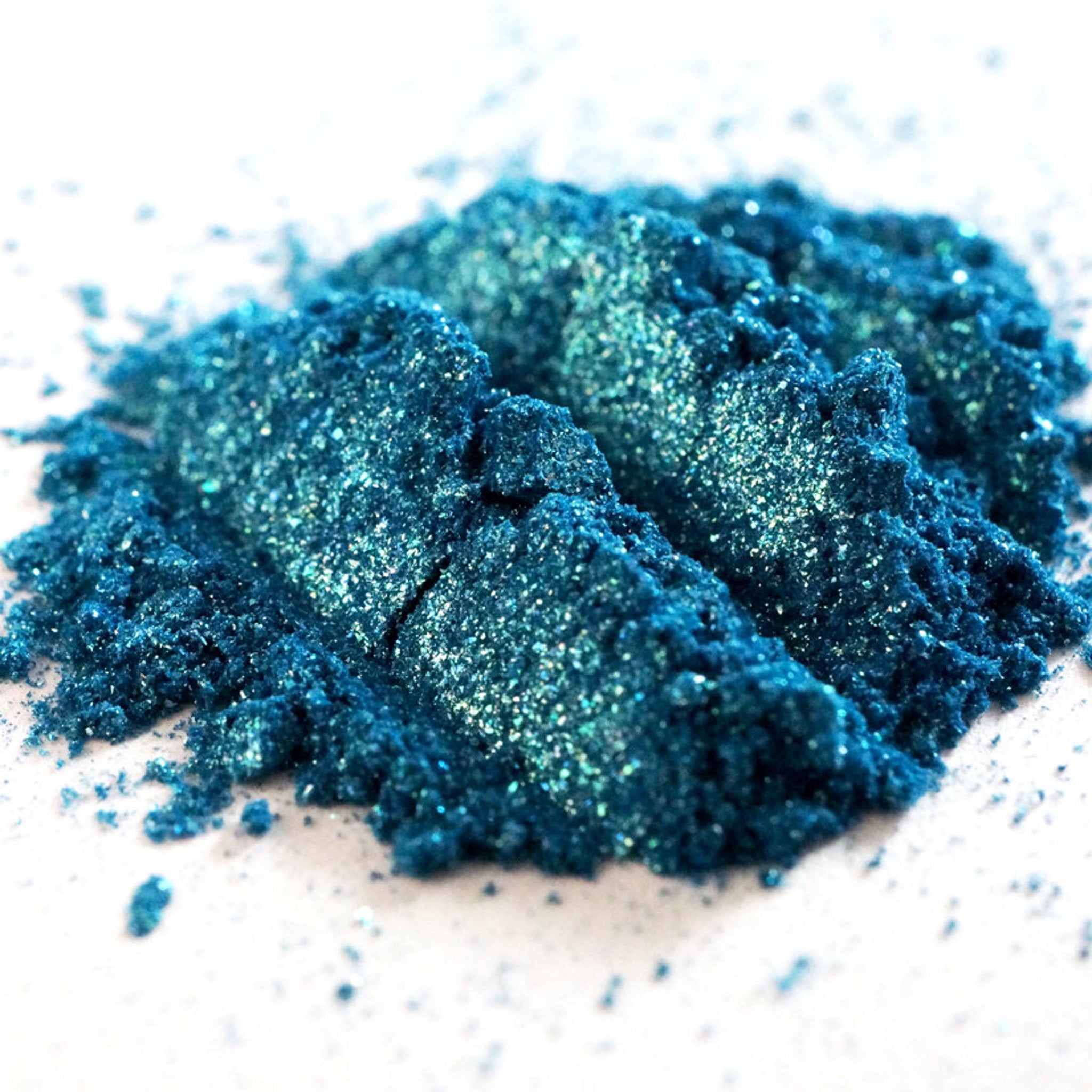 Close-up of teal shimmer loose mineral eyeshadow with turquoise and green glitter particles sparkling in light