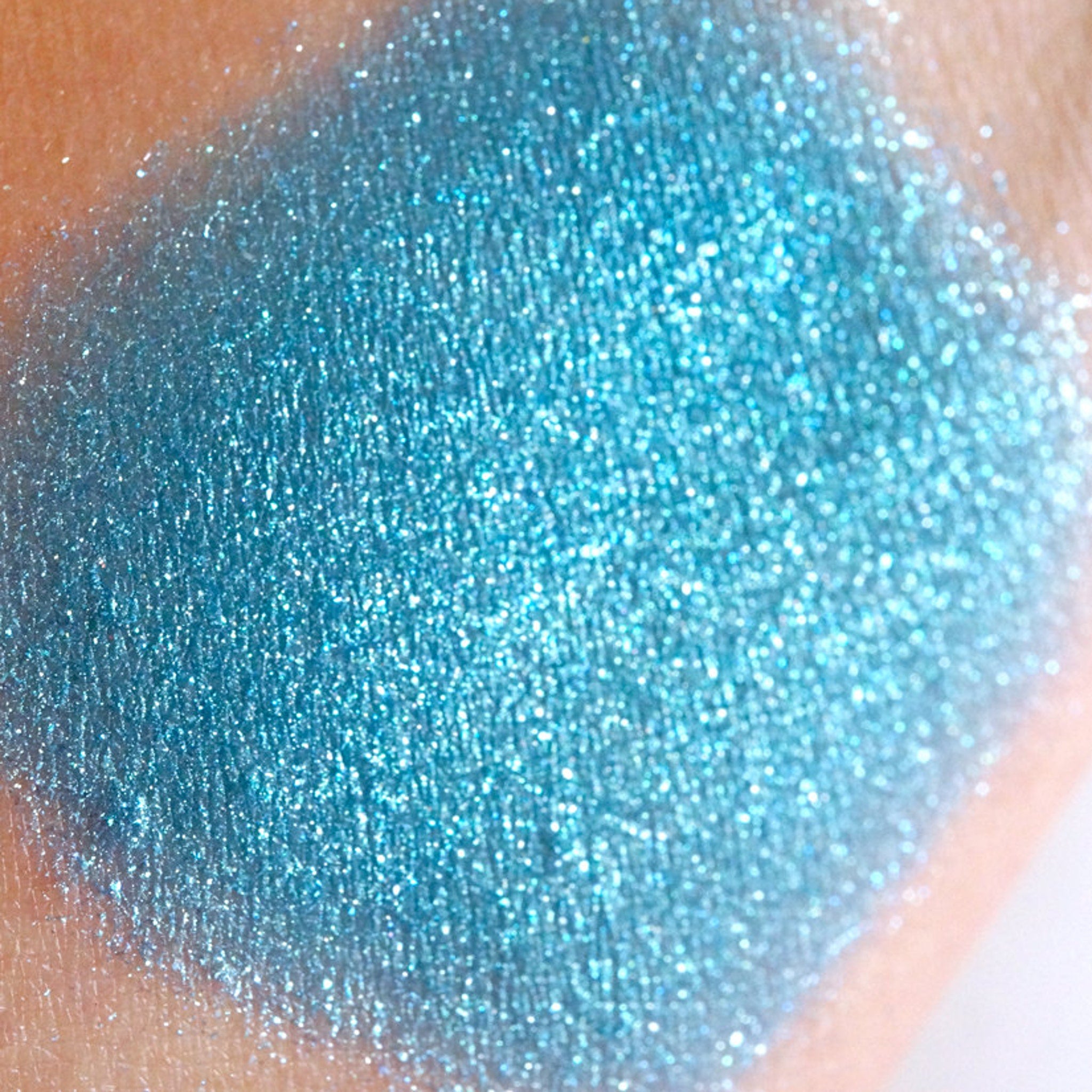 Side view of loose mermaid blue eyeshadow with teal shimmer and turquoise-green glitter particles catching light