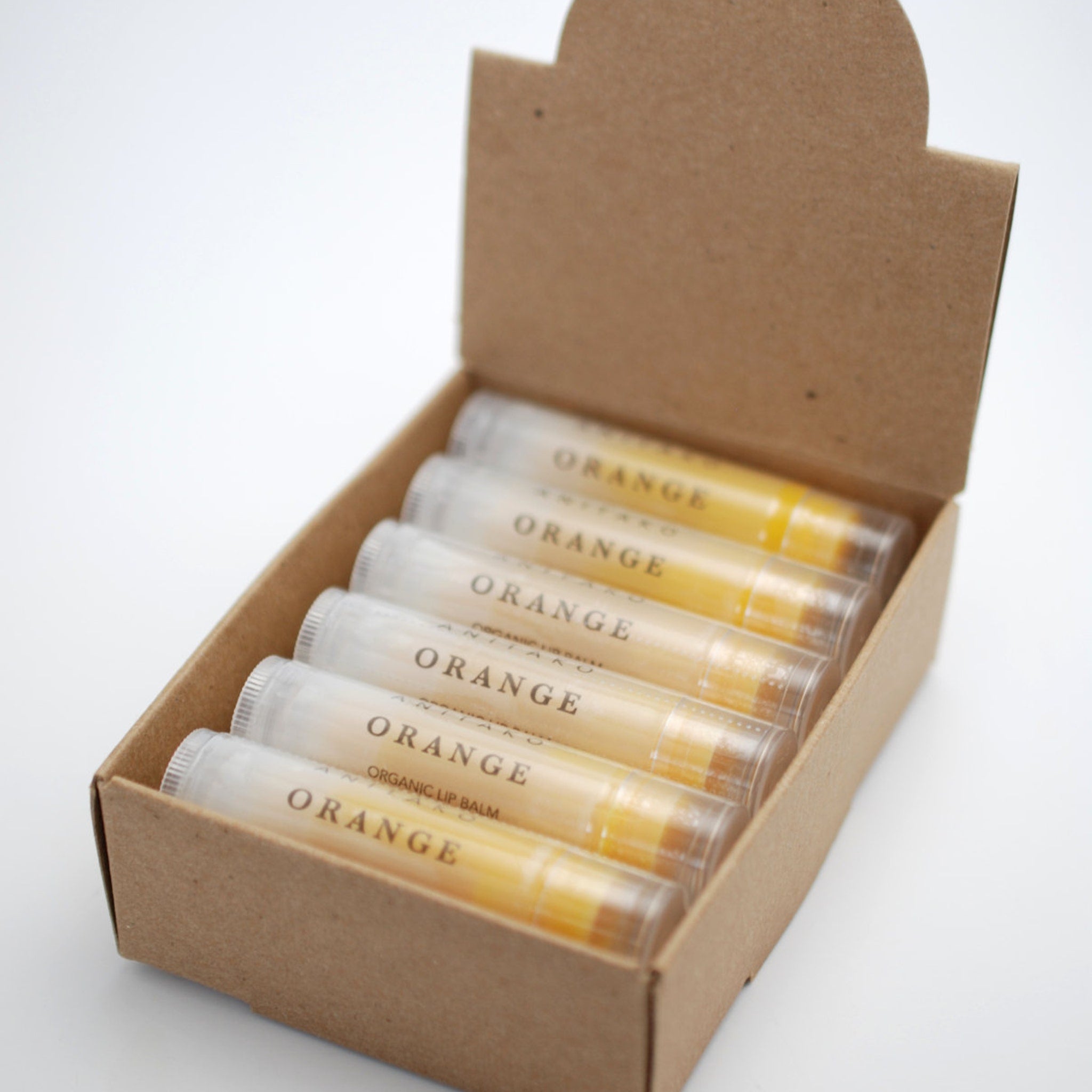 Lip balm tubes in a cardboard box, clear tubes with orange balm and white labels