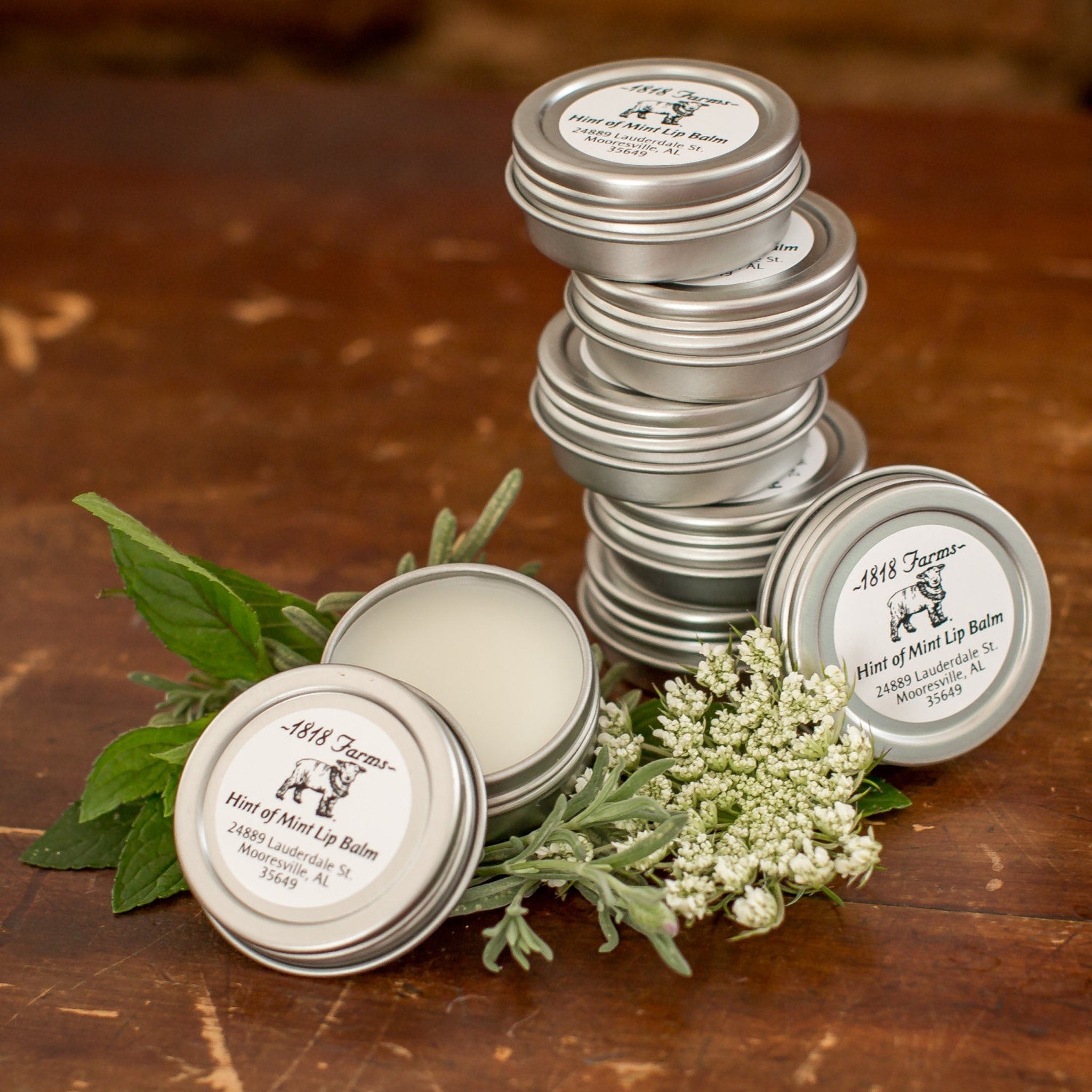 Lip balm tins, silver metal containers, 1818 Farms branding, stacked and arranged with greenery