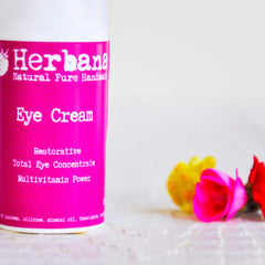 Eye cream in pink and white bottle with "Herbana" brand name and flowers in background