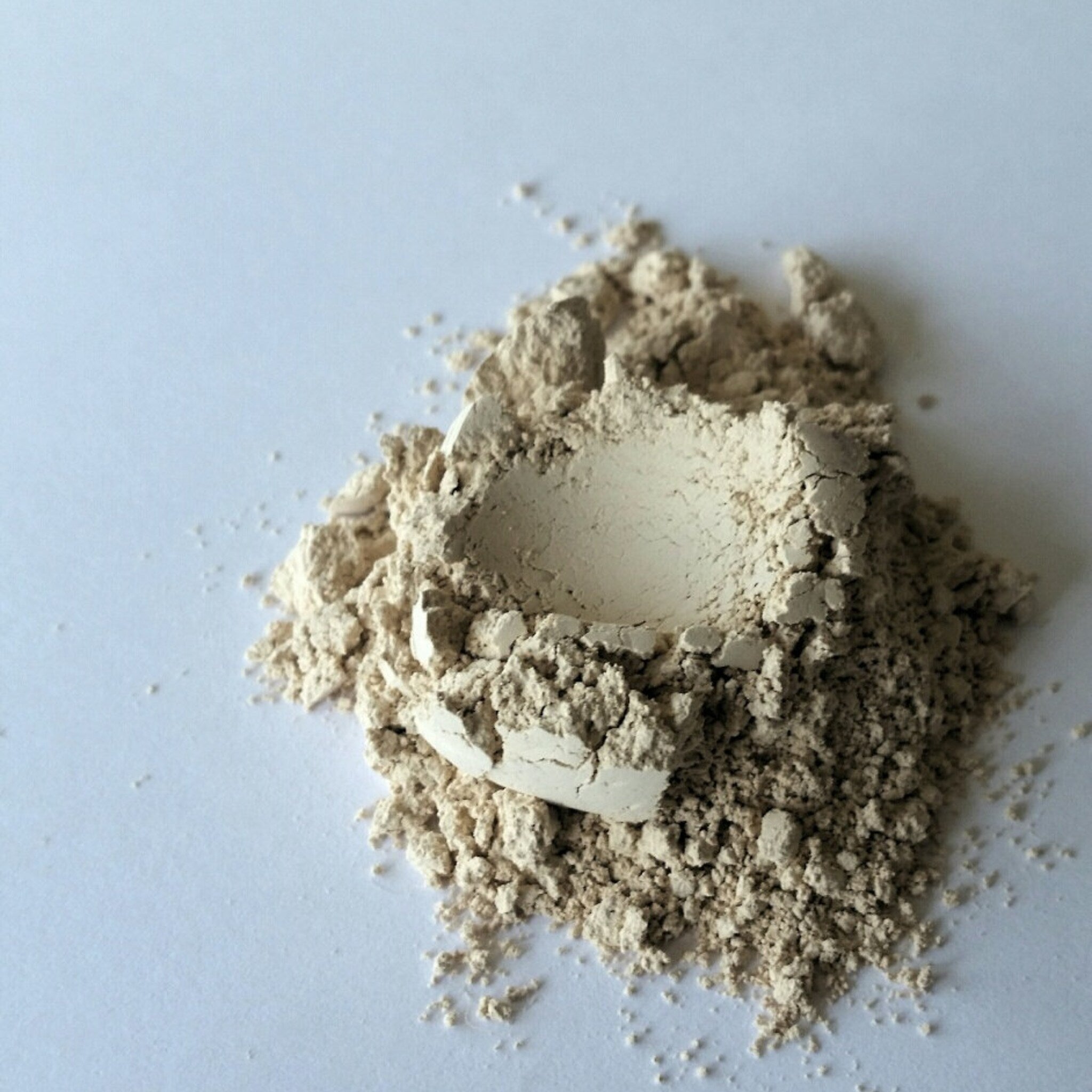Powdered substance, light beige color, granular texture, piled on white surface