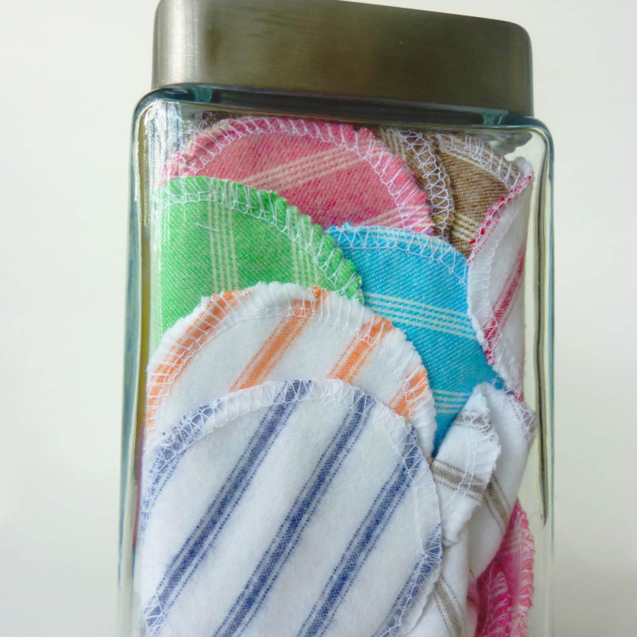 Reusable face rounds with assorted colors, striped and plaid patterns, and white stitching in glass jar