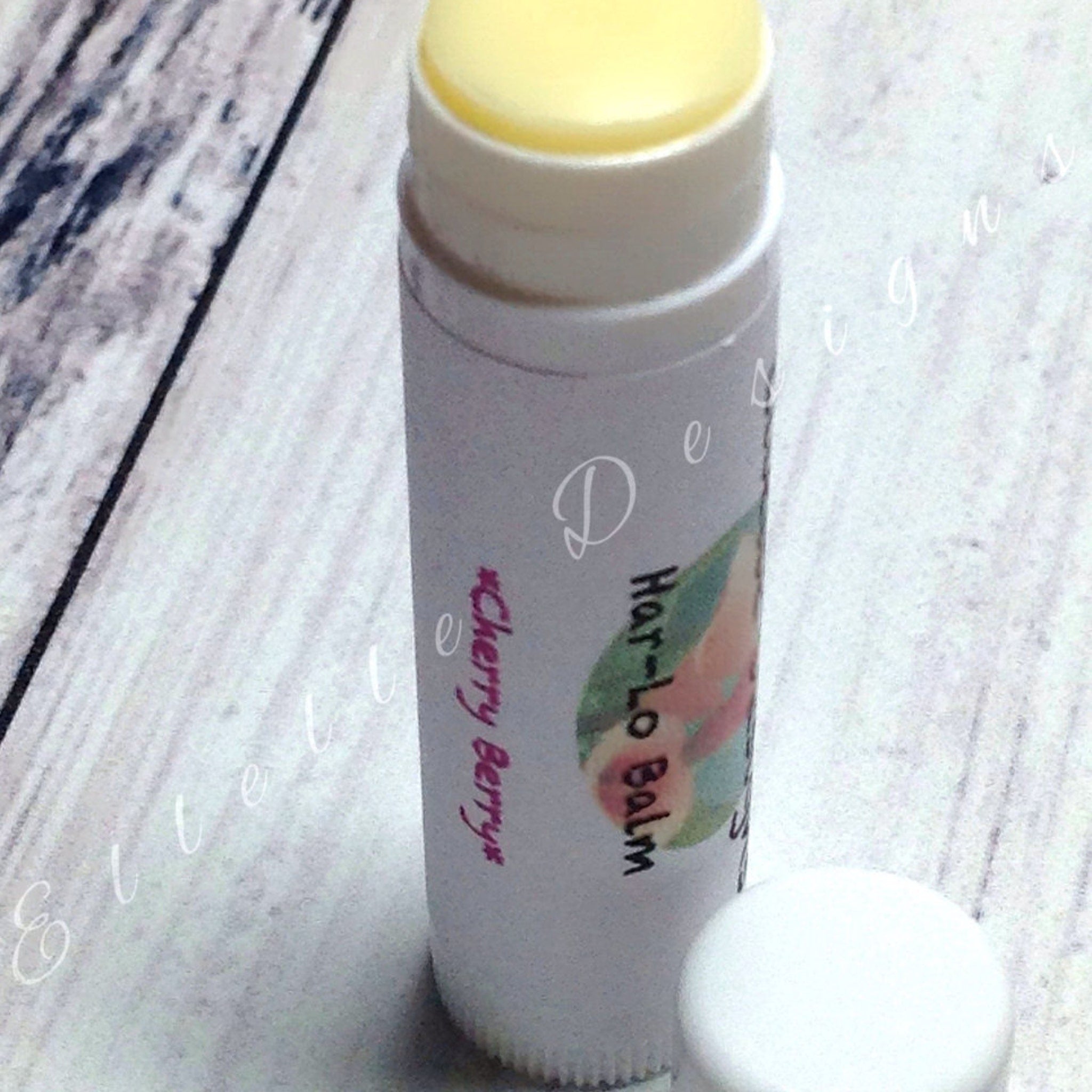 Lip balm tube with white and pink text, yellow balm, and white cap on wooden surface