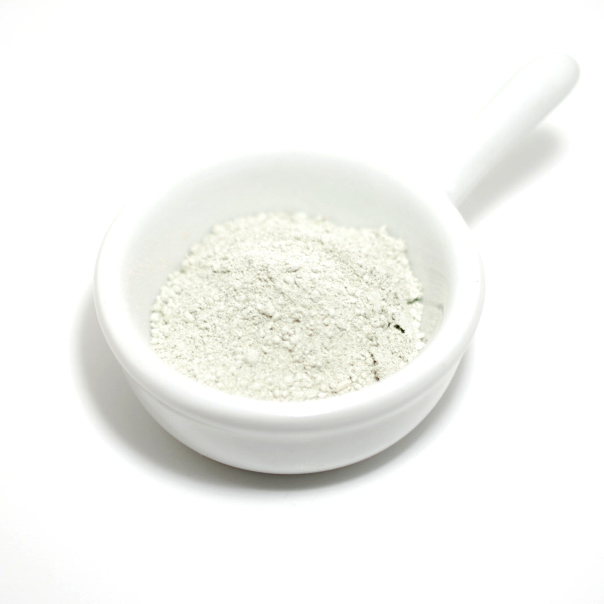 Powdered product in white ceramic bowl, pale green powder, white handle, isolated on white background