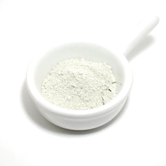 Powdered product in white ceramic bowl, pale green powder, white handle, isolated on white background